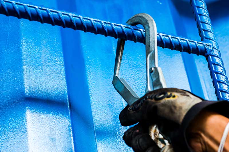 Hand mit Karabiner an blauem Stahlseil